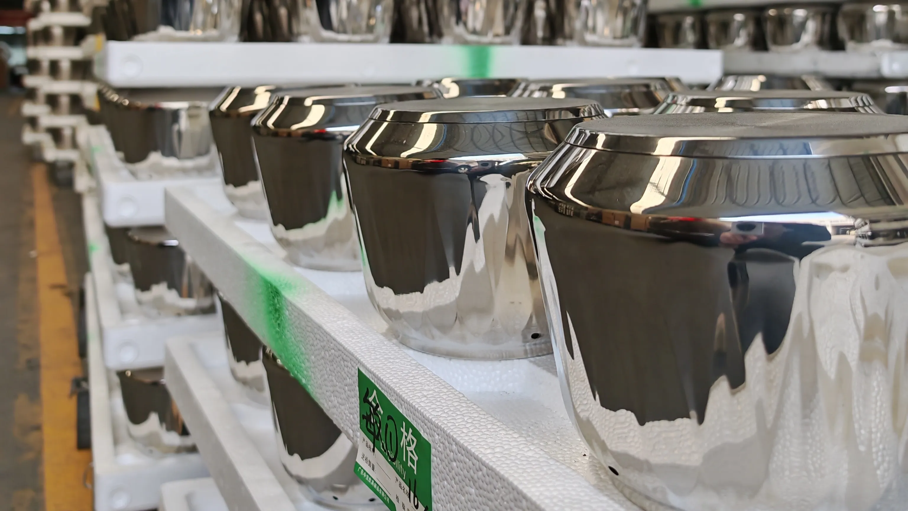 Mirror-polished stainless steel pot bodies staged on white racks with quality-control labels in a Chinese cookware factory