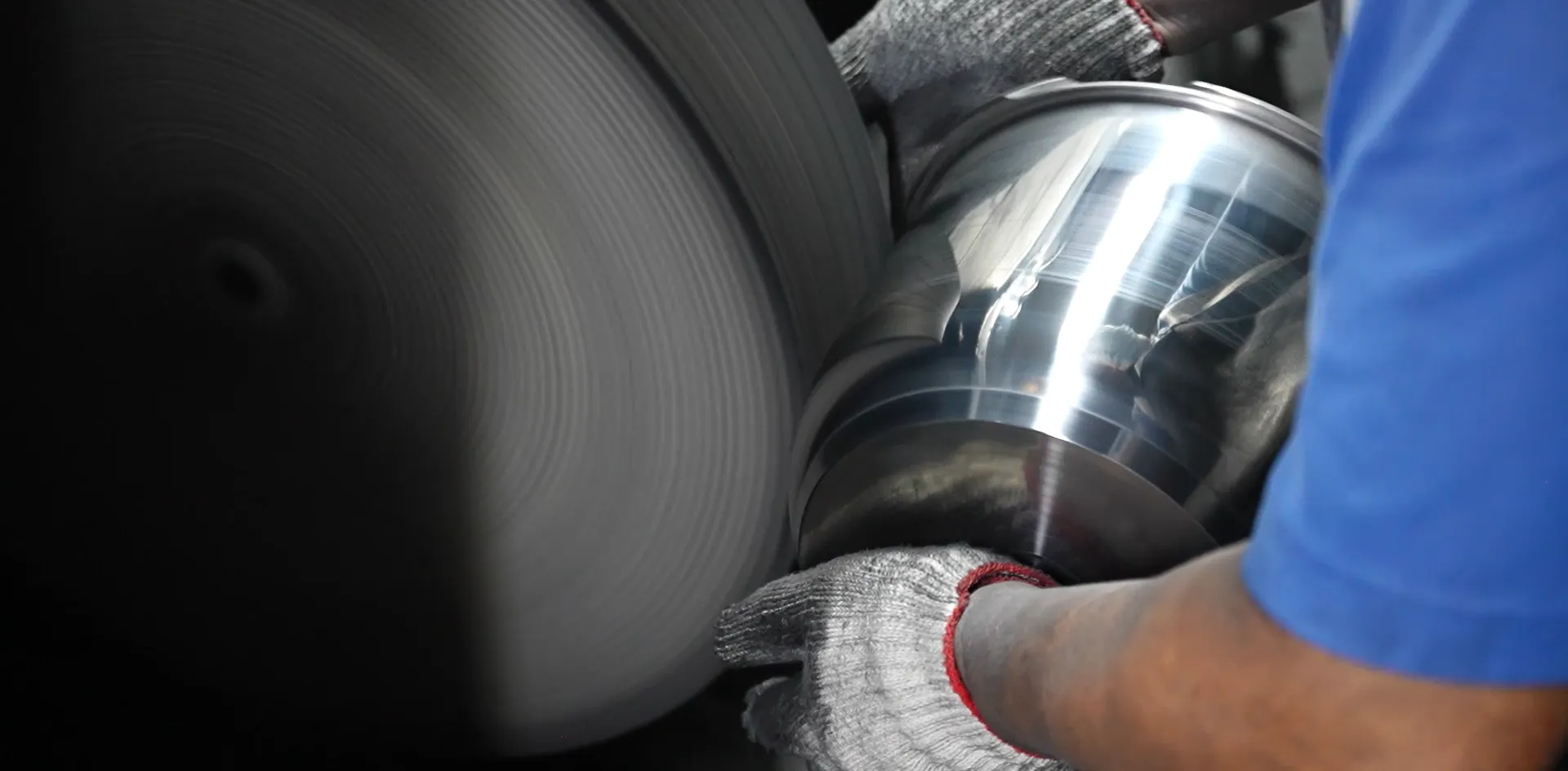 Factory operator hand-polishing a stainless steel cookware body against a belt sander, the finishing step that determines sample quality