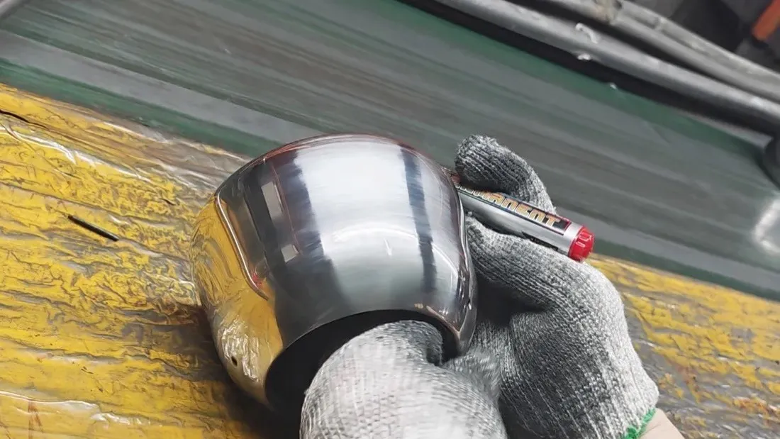 A gloved worker marking a polished stainless steel kettle body on the finishing line